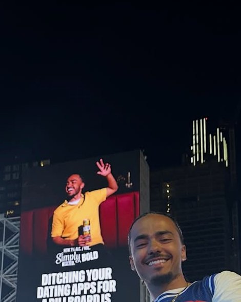 Jailen James at night in downtown Toronto in front of the Simply Spiked billboard he appears on